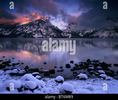 Ein rosa Sonnenaufgang Spiegelbild auf einem zugefrorenen See Jenny zeigt erste Licht durch ein Wintersturm im Grand-Teton-Nationalpark, Wyoming. Stockfoto