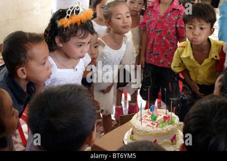 Eine 6-jährige Asiatin bläst 6 Kerzen auf einem Geburtstagskuchen mit Freunden glückliche Schulkinder in Kambodscha. Stockfoto