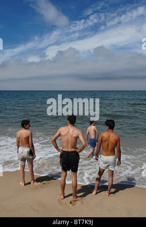 Vier Jugendliche stehen am Meer mit dem Rücken zur Kamera Stockfoto