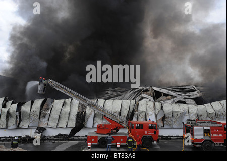 Feuerwehr auf ein Feuerwehrauto Ausziehleiter Löschangriff eine massive Fabrik inmitten dichten Rauch Stockfoto