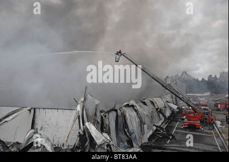 Feuerwehr auf eine Ausziehleiter Löschangriff eine massive Fabrik inmitten dichten Rauch Stockfoto