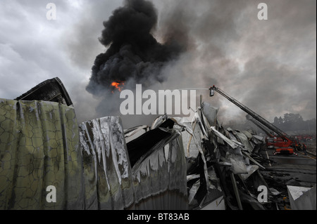 Feuerwehr auf eine Ausziehleiter Löschangriff eine massive Fabrik inmitten dichten Rauch Stockfoto