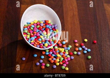 Farbige Schokolinsen in weiße Schüssel auf Holztisch Stockfoto