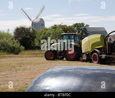 Ein moderner Traktor schneidet Heu vor der alten Bockwindmühle in Großbritannien. Stockfoto