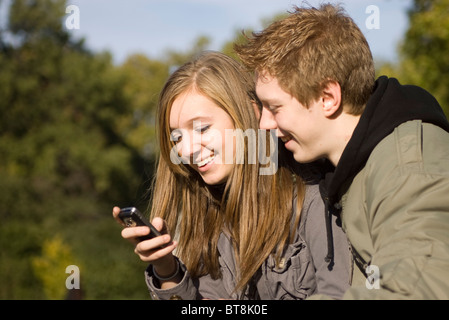 Teenager-Jungen und Mädchen im Park Blick auf Handy zusammen, teilen, Lächeln Stockfoto