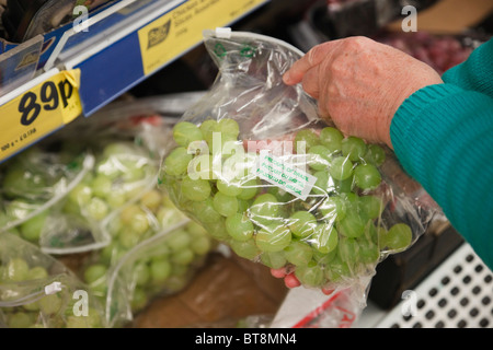 Frau Wahl ein Paket von billigen Preisen Trauben in einer Plastiktüte auf einen LIDL Supermarkt Regal angezeigt. Großbritannien Großbritannien Stockfoto