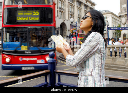 orientalische Frau am Oxford Circus in London Kartenlesen mit roten Doppeldecker-Bus im Hintergrund - Bewegungsunschärfe Stockfoto