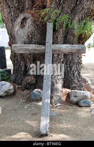 An einem Kalifornien-Pfefferbaum in einem indischen Friedhof an der MIssion San Antonio de Pala gelehnt Holzkreuz Stockfoto