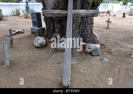 An einem Kalifornien-Pfefferbaum in einem indischen Friedhof an der MIssion San Antonio de Pala gelehnt Holzkreuz Stockfoto