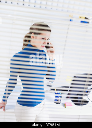 Geschäftsfrau am Telefon hinter Jalousien Stockfoto