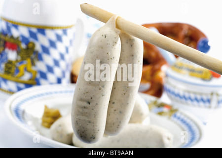 Bayerische Weißwurst hängend von einem Löffel zu behandeln, im hinteren verschwommen Bierkrug, Brezel, Senf-Topf Stockfoto