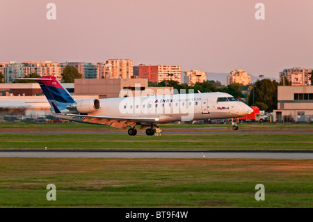 Eine Dreieckschaltung (SkyWest Airlines) CRJ-200ER Regional Jet Flugzeug landet in Vancouver International Airport (YVR) bei Sonnenuntergang. Stockfoto