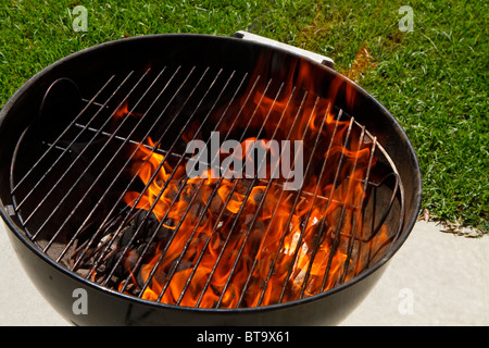 Flammen in einer gerechten beleuchtet Barbeque-Grill auf eine äußere konkrete Terrasse an einem sonnigen Tag im Sommer. Keine Lebensmittel gebracht zum Kochen noch. Stockfoto