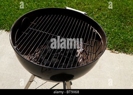 Ein Barbecue-Grill auf eine äußere konkrete Terrasse an einem sonnigen Tag im Sommer. Die Holzkohle hat ordentlich in der Mitte aufgetürmt. Stockfoto