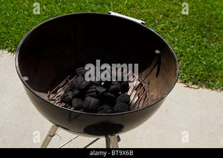 Ein Barbecue-Grill auf eine äußere konkrete Terrasse an einem sonnigen Tag im Sommer. Die Holzkohle hat ordentlich in der Mitte aufgetürmt. Stockfoto