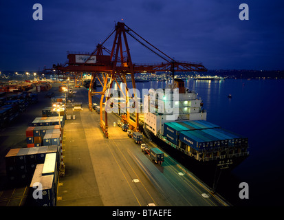 Riesige Kräne laden ein Container Frachtschiff am Wasser während des Sonnenuntergangs am Hafen von Seattle, Washington, USA. Stockfoto