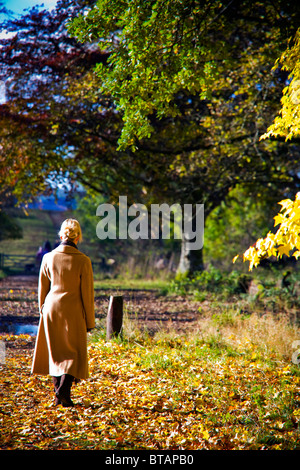 FRAU ZU FUß IM COUNTRY PARK IM OKTOBER TRÄGT EINEN WARMEN WINTERMANTEL UND STIEFEL Stockfoto