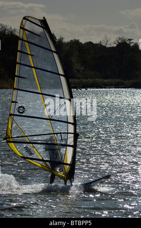 Ein Windsurfer Windsurfen auf dem Wasser, Silhouette gegen tiefstehende Sonne. Stockfoto