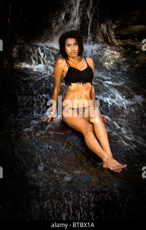 Schöne Frau sitzt auf einem Felsen vor einem Wasserfall Stockfoto