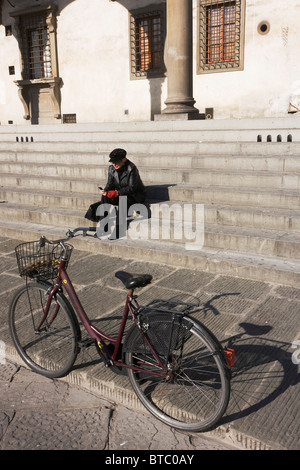 Frau nutzt Mobile rief beim Sitzen in der Nähe von Fahrrad auf Stufen des öffentlichen Gebäude in Piazza Di Annunziata in Florenz. Stockfoto