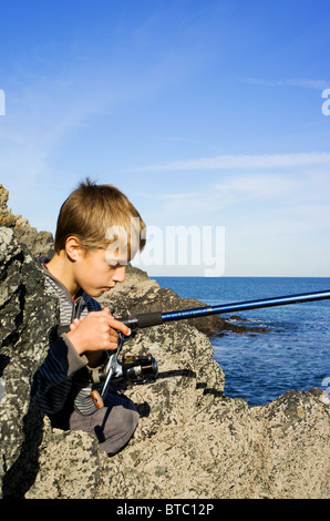 ein kleiner Junge Angeln von den Felsen auf der Heiligen Insel im Angelsey, North Wales, UK Stockfoto