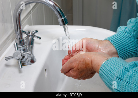 Eine ältere Frau reinigt, indem sie die Hände gründlich unter fließendem Leitungswasser in einem Handbecken waschen, um sich vor Krankheiten zu schützen. England Großbritannien Stockfoto