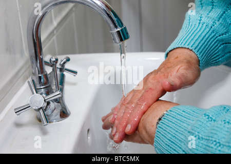 Eine ältere Frau reinigt, indem sie die Hände gründlich unter fließendem Leitungswasser in einem Handbecken waschen, um sich vor Krankheitskeimen zu schützen. England Großbritannien Stockfoto