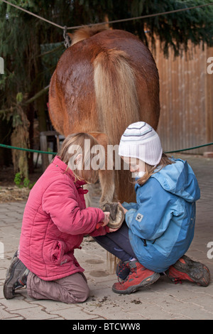 zwei kleine Mädchen, die Reinigung der Hufe eines Ponys Stockfoto