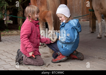 zwei kleine Mädchen, die Reinigung der Hufe eines Ponys Stockfoto