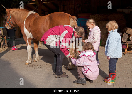 kleine Mädchen, die Reinigung der Hufe eines Ponys von ihrer Reitlehrerin betreut Stockfoto