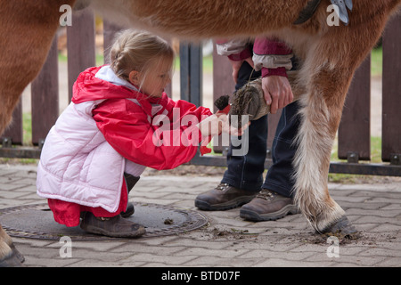 kleine Mädchen, die Reinigung der Hufe eines Ponys Stockfoto