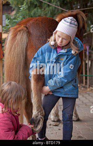 zwei kleine Mädchen, die Reinigung der Hufe eines Ponys Stockfoto