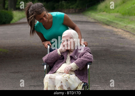 junge Frau, die alte Dame im Rollstuhl schieben Stockfoto