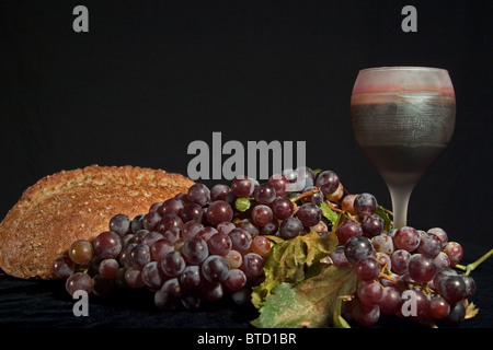 Stillleben mit Brot, rote Weintraube und Glas Rotwein auf schwarzem Hintergrund. Stockfoto