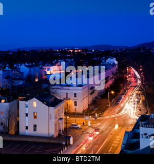 Regency Buildings und beleuchtete Straße im Stadtzentrum von Cheltenham in der Abenddämmerung mit Ampelpfaden, Gloucestershire, England. Stockfoto