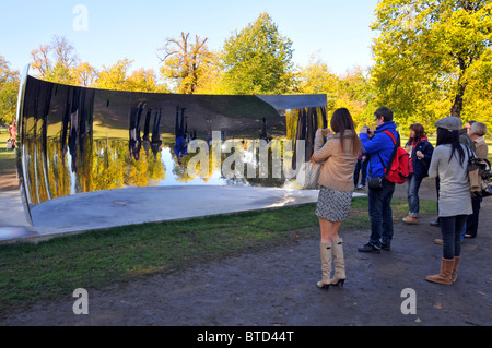 Besucher, die in den Kensington Gardens sind, sehen reflektierte Bilder von sich selbst in einem der Anish Kapoor Sky Mirrors C Curve London England UK Stockfoto