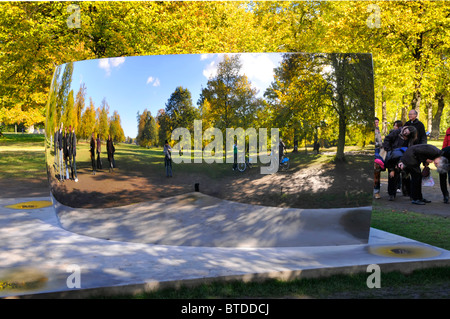 Besucher, die in den Kensington Gardens sind, sehen reflektierte Bilder von sich selbst in einem der Anish Kapoor Sky Mirrors C Curve London England UK Stockfoto