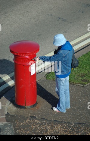 Frau Entsendung Postkarte in traditionellen Royal Mail rot Briefkasten, Cromer, Norfolk, England, UK Stockfoto