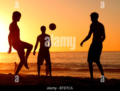 Junge weiße Erwachsene Männer Fußball spielen auf einem Strand in der Abenddämmerung Stockfoto