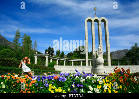 Frau sitzt auf einer Bank am Franschhoek Denkmal mit bunten Blumen im Vordergrund Stockfoto