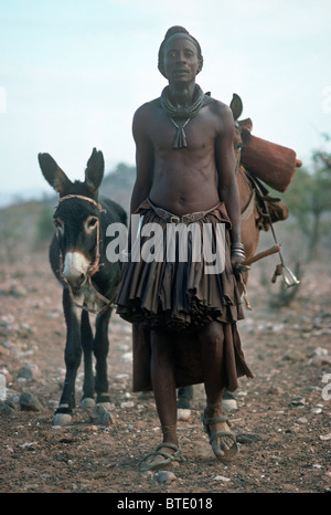 Himba-Mann gekleidet in traditioneller Kleidung führt ein Pferd und Esel Stockfoto