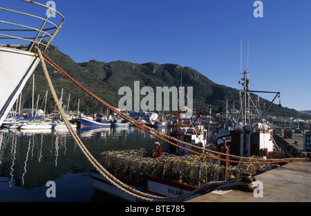 Malerische Aussicht auf den Hafen von Hout Bay mit einem Schiff vor Anker in den Vordergrund und Krebse Käfigen auf einem Boot Stockfoto