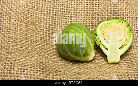 Ganze und aufgeschnittene Rosenkohl von niedrigen Perspektive auf hessischen sack Hintergrund. Stockfoto