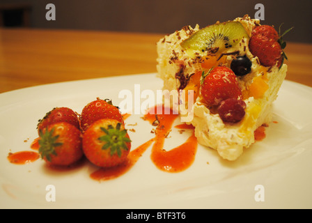 frische Frucht Pavlova mit Erdbeersauce Stockfoto