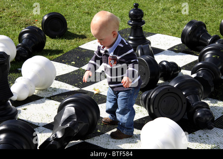 Kleiner Junge spielt mit großen Schachfiguren im Freien im Vereinigten Königreich Stockfoto
