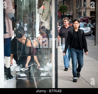 Ein Mitarbeiter passt das Schaufenster eines H & M-Stores in New York, als Passanten vorbeigehen Stockfoto