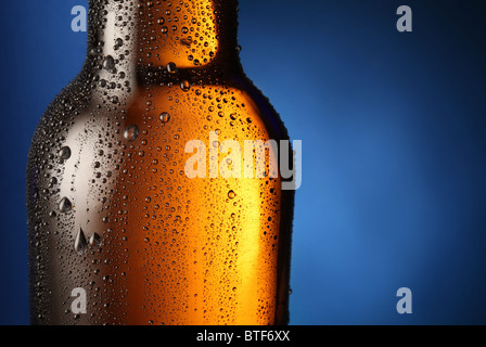 Eine Flasche Bier mit Tropfen auf einem blauen Hintergrund. Hautnah Teil der Flasche. Stockfoto