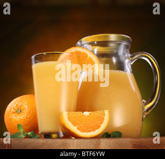 Stillleben: Orangen, Glas Saft und Krug voller Saft auf einem Holztisch. Stockfoto