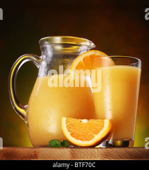 Stillleben: Orangen, Glas Saft und Krug voller Saft auf einem Holztisch. Stockfoto