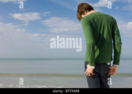 Junge Mann stand am Strand mit Kopf nach unten, Rückansicht Stockfoto